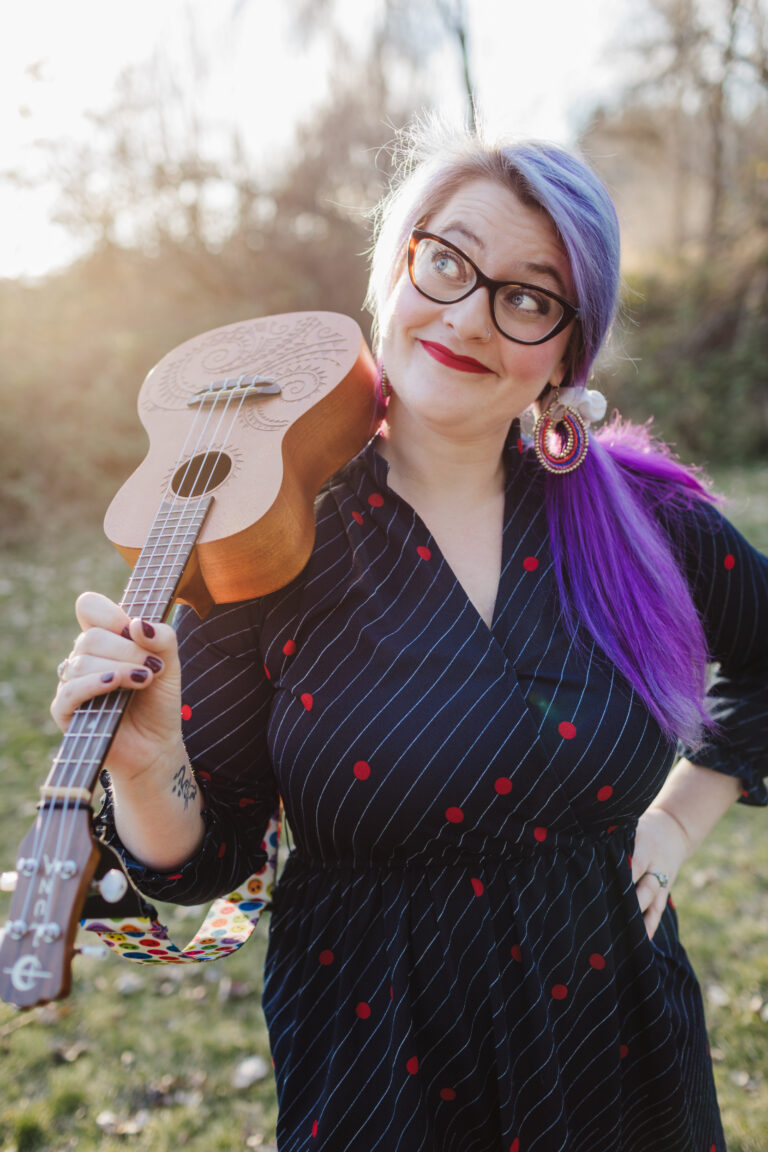 Holly gazing upwards with a smirk and holding ukulele on her shoulder
